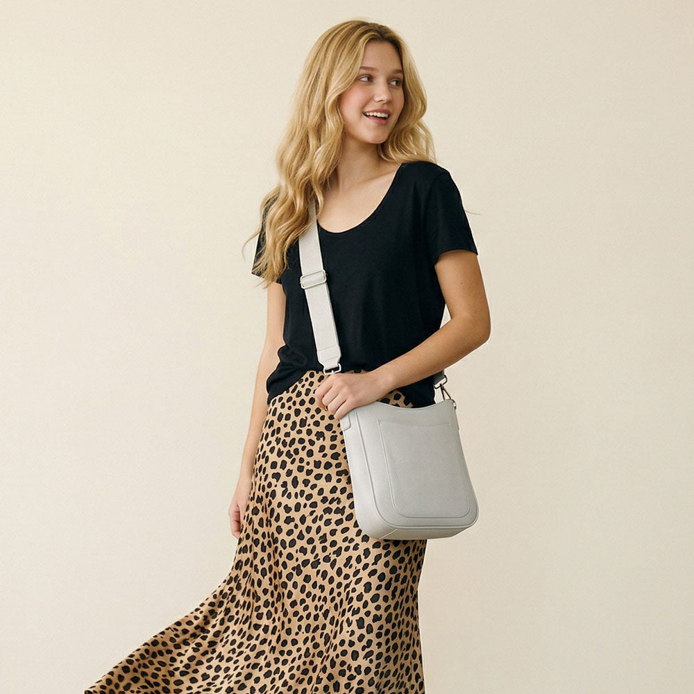 Woman wearing a cream crossbody bag wearing a black top and leopard print skirt on a beige background