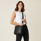 Woman holding a black handbag with grommets on the front against a beige background