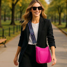 Woman in a park wearing sunglasses, black blazer, white shirt, and pink handbag.