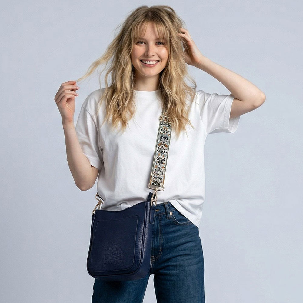 Woman wearing a navy blue handbag with an embellished strap against a light gray background