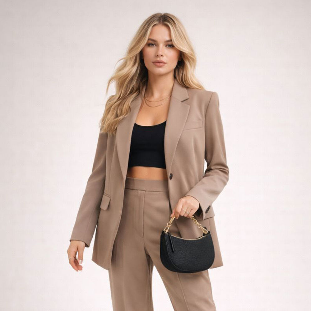 Woman in a beige suit holding an ahdorned black handbag on a white background