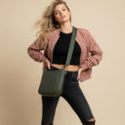 Woman wearing a army crossbody bag against a beige background