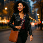 Woman walking outside in the early evening in the city, wearing a camel crossbody and striped bag strap