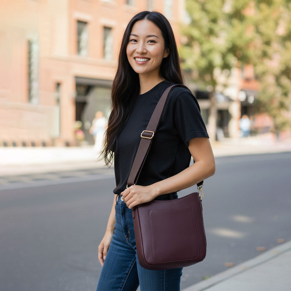 Woman holding a maroon crossbody bag on a city street