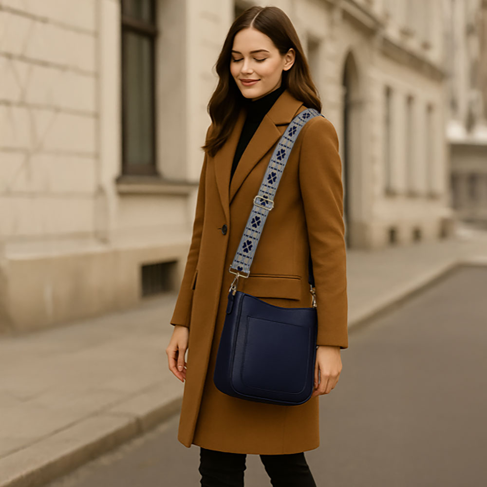 Woman posing on the street wearing a navy crossbody bag and embroidered bag strap. 
