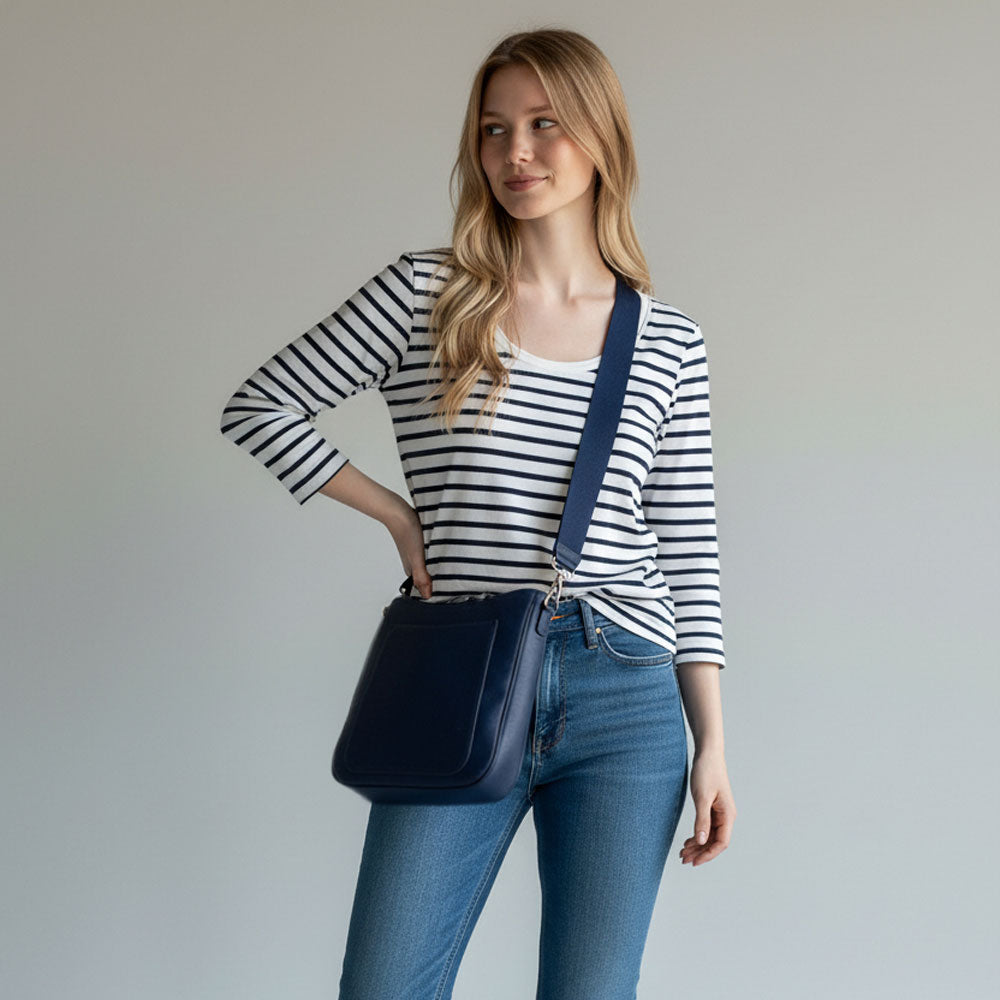 Woman wearing a striped shirt and jeans with a navy bag on a plain background