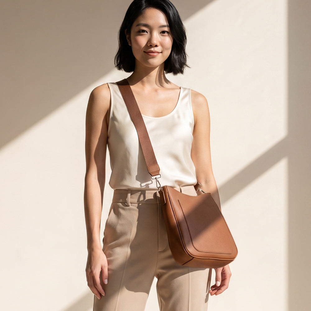Woman wearing a Camel colored crossbody bag on a neutral background