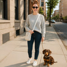 Woman walking a small dog on a city street. Wearing a cream crossbody bag.
