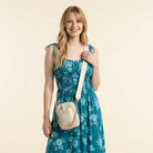 Woman in a blue floral dress wearing a cream handbag against a beige background