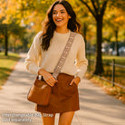 Woman walking outdoors in a park with a camel vegan leather bag and beige sweater.