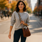 Woman posing on a city sidewalk with a brown crossbody bag and printed animal bag strap.