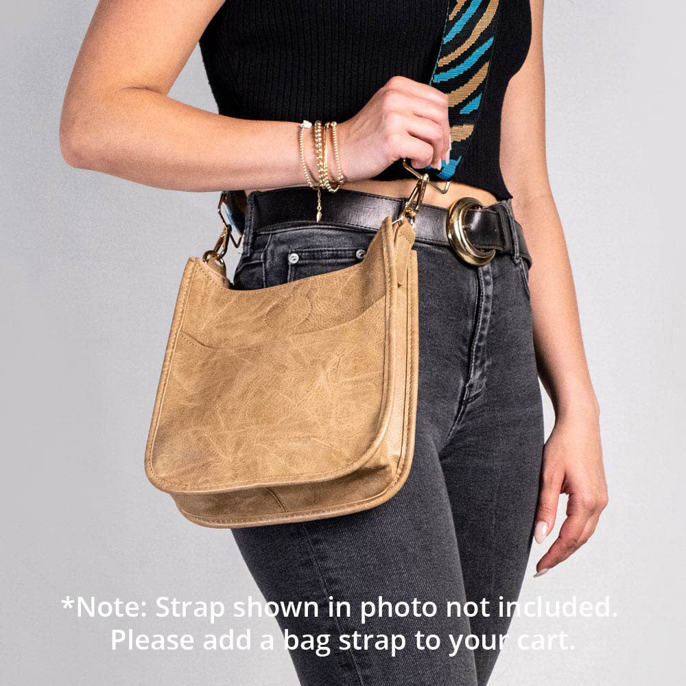 Person holding a brown leather handbag against a gray background. Text: Note: Strap shown in photo not included.  Please add a bag strap to your cart.