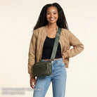 Woman wearing a army crossbody bag with an interchangeable strap on a beige background