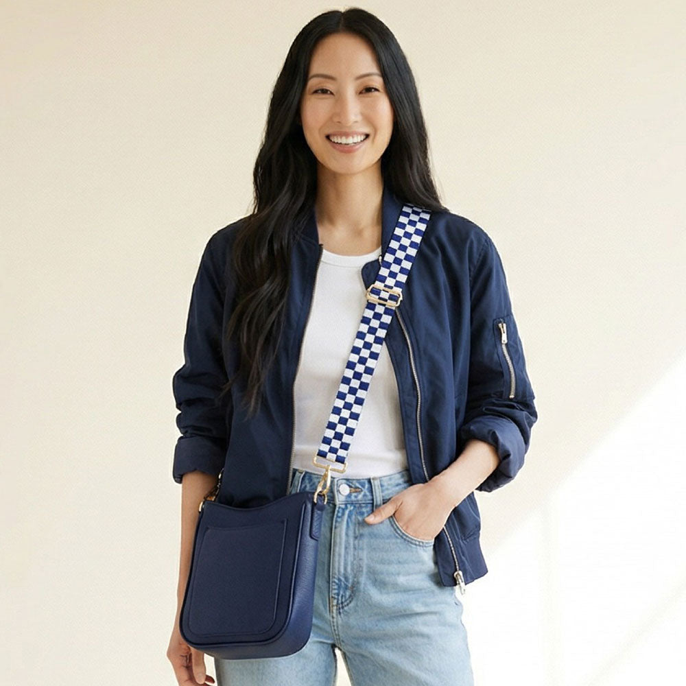 Woman wearing a navy blue jacket with a checkered strap, wearing a navy bag against a beige background