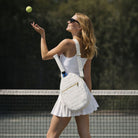Woman on a tennis court with a white tennis racket bag, holding a tennis ball.