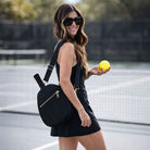 Woman holding a yellow tennis ball on a tennis court with a black pickleball paddle bag.