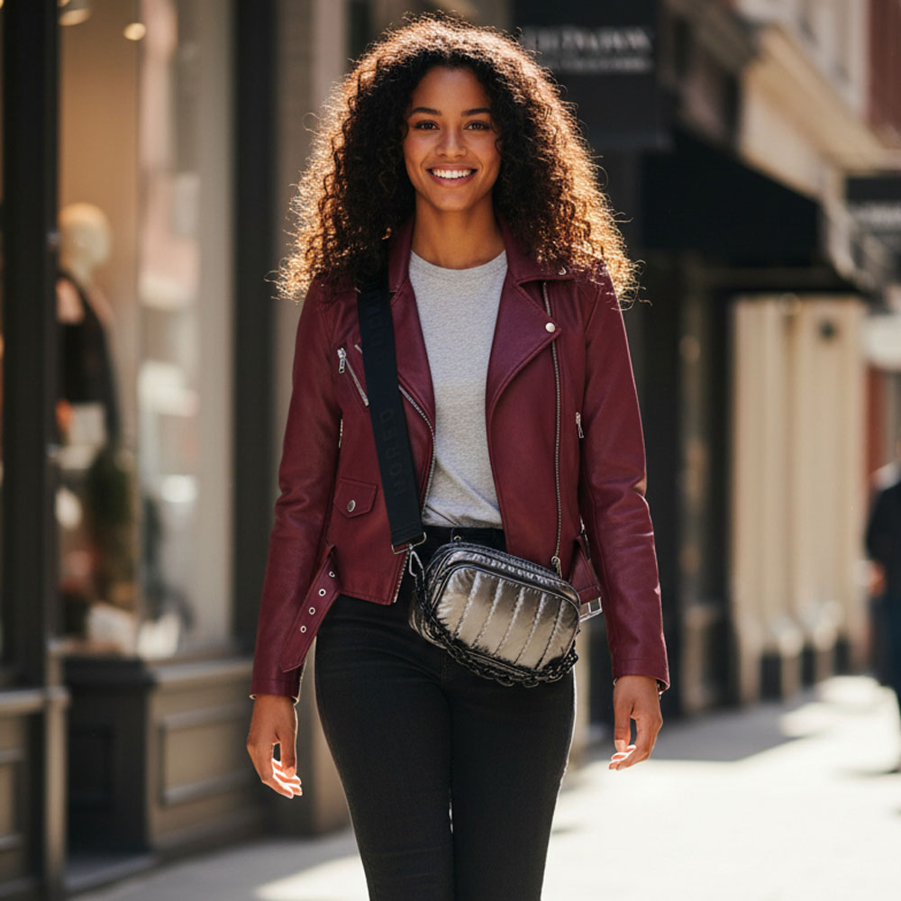 Woman wearing a maroon leather jacket and black pants on a city street. Wearing a pewter crossbody bag.
