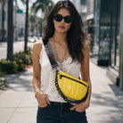 Woman walking on a sidewalk wearing a yellow quilted bag and sunglasses.