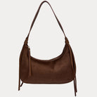 A chocolate vegan suede shoulder bag with a vegan leather details, shown against a light gray 