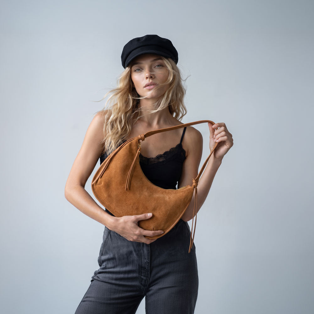 Woman holding a vegan suede shoulder bag with vegan leather details in camel.  Set on a light grey background