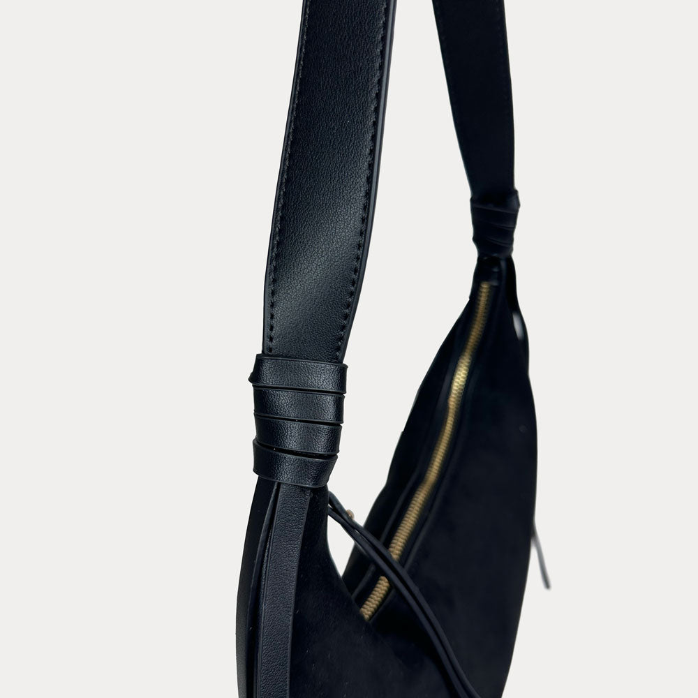 Close-up of a black vegan leather shoulder bag, showing the strap detail against a light gray background.