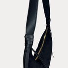Close-up of a black vegan leather shoulder bag, showing the strap detail against a light gray background.