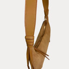 A close-up of a camel vegan leather shoulder bag strap, set against a plain light gray background.