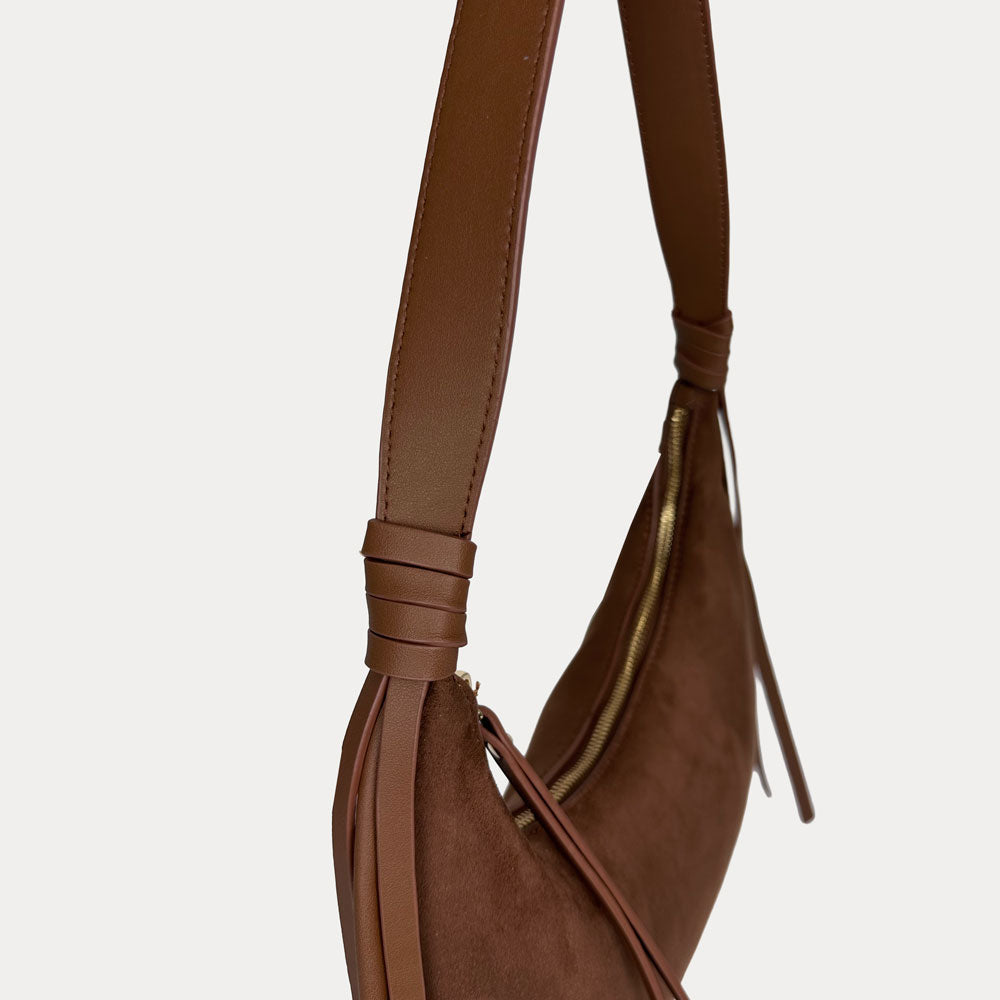 A close-up side view of a chocolate vegan suede with vegan leather details shoulder bag, set against a plain light gray background.