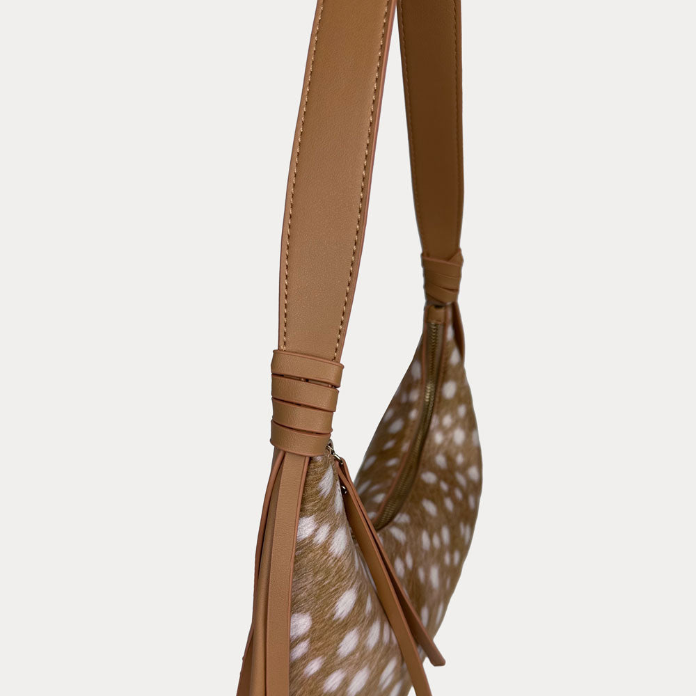 Close-up of a shoulder bag with  camel vegan leather strap and deer print body, shown against a light gray background.