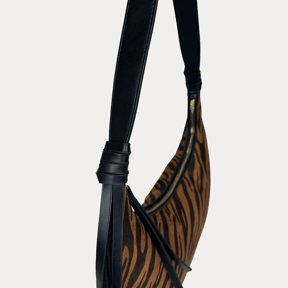 A close-up of a shoulder bag featuring a brown and black tiger-stripe patterned body with a black vegan leather strap.