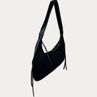 A black vegan suede shoulder bag with a vegan leather strap and hanging tassels, shown against a light gray background.