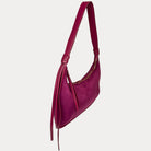 A burgundy vegan suede shoulder bag with vegan leather strap and tassel detail, shown from a side profile view against a light gray background.