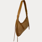 A camel vegan suede shoulder bag with a vegan leather strap and hanging fringe details, shown from a side profile on a light gray background.