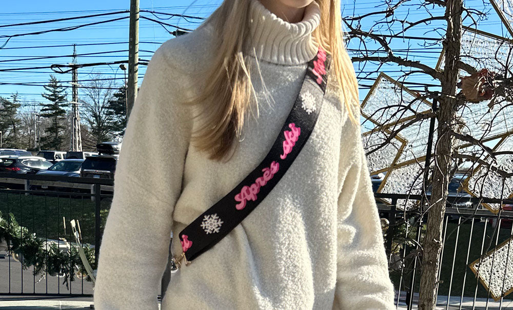Person wearing a white sweater with a black strap featuring pink text and floral designs.