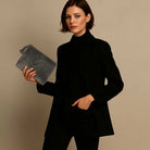 Woman in a black coat holding a gray clutch against a beige background