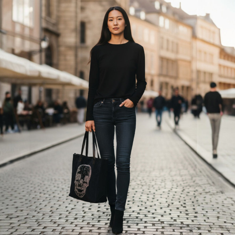 Woman in black outfit holding a black tote bag with a face design on a city street.