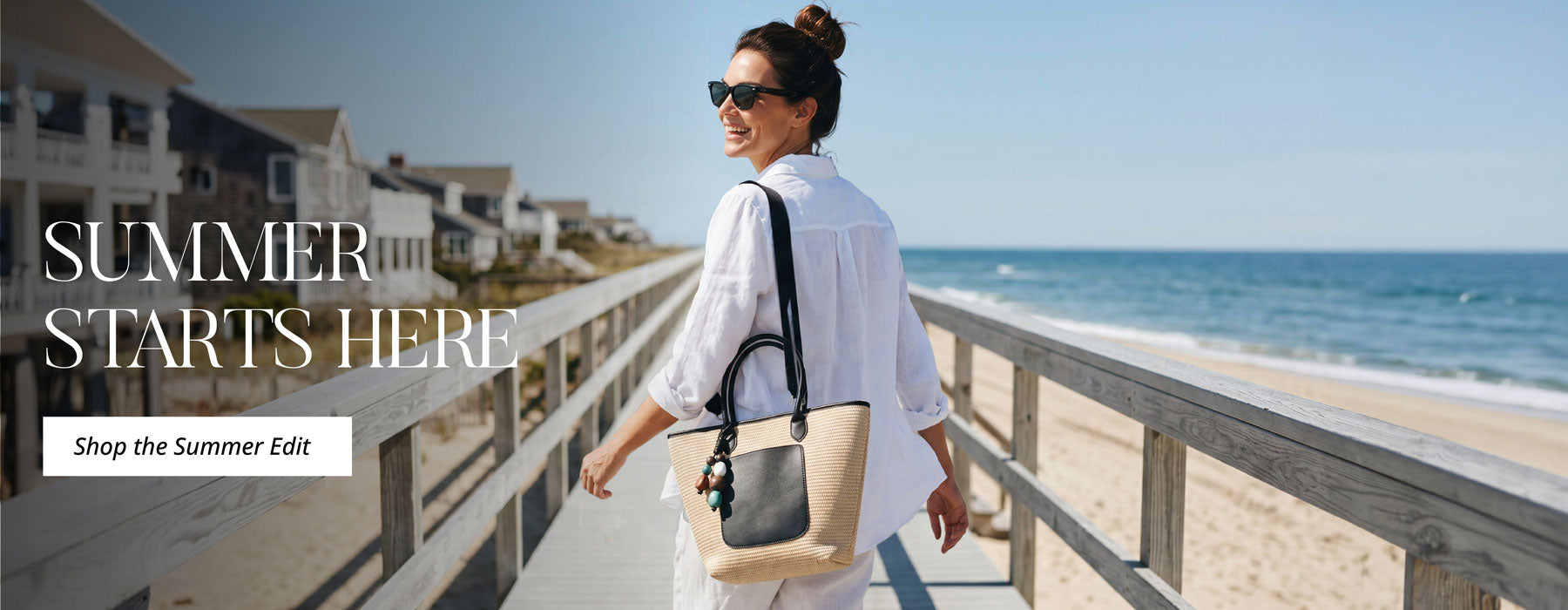 Woman walking on a boardwalk by the beach with a Raffia Tote with text 'Summer Starts Here' and 'Shop the Summer Edit'.